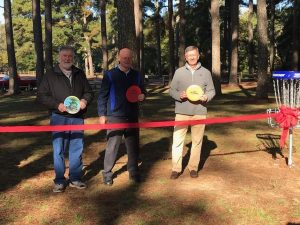 Three men smiling holding discs for the ribbon cutting of the new disc golf course at McFarland Park in Florence, Alabama.